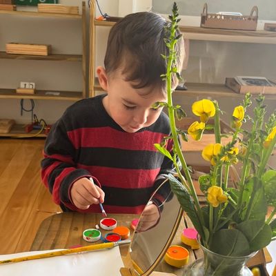 Menino pintando com tinta ao lado de um vaso de flores amarelas